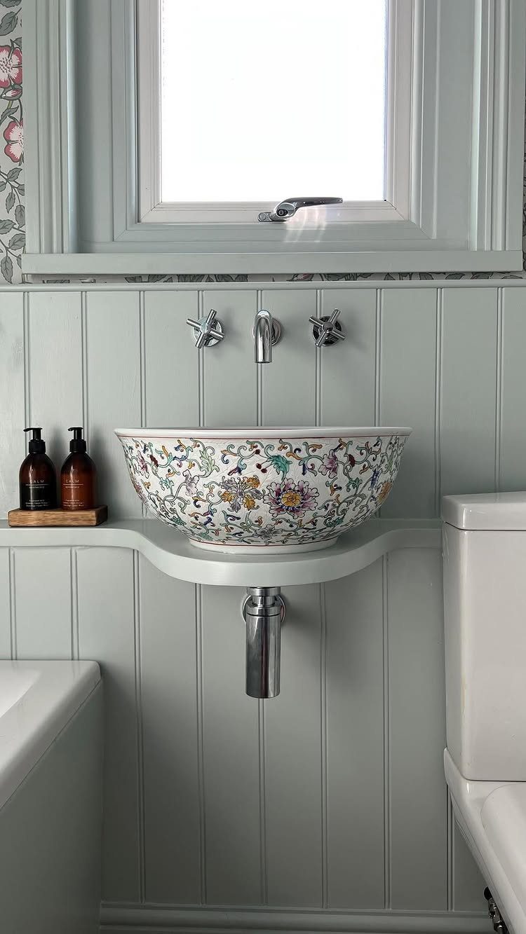 Floral ceramic vessel sink against light green paneled walls in a bathroom