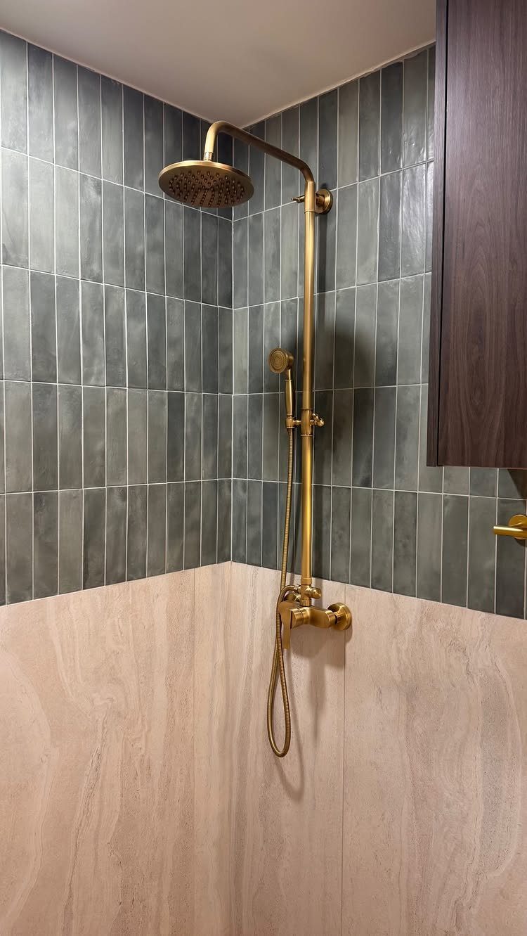 Dark green vertical tiles and beige stone walls with gold shower fixtures.