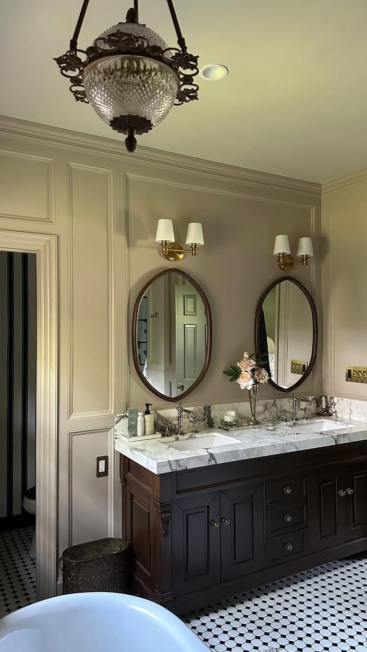 Dark wood vanity with marble top and oval mirrors in a beige bathroom