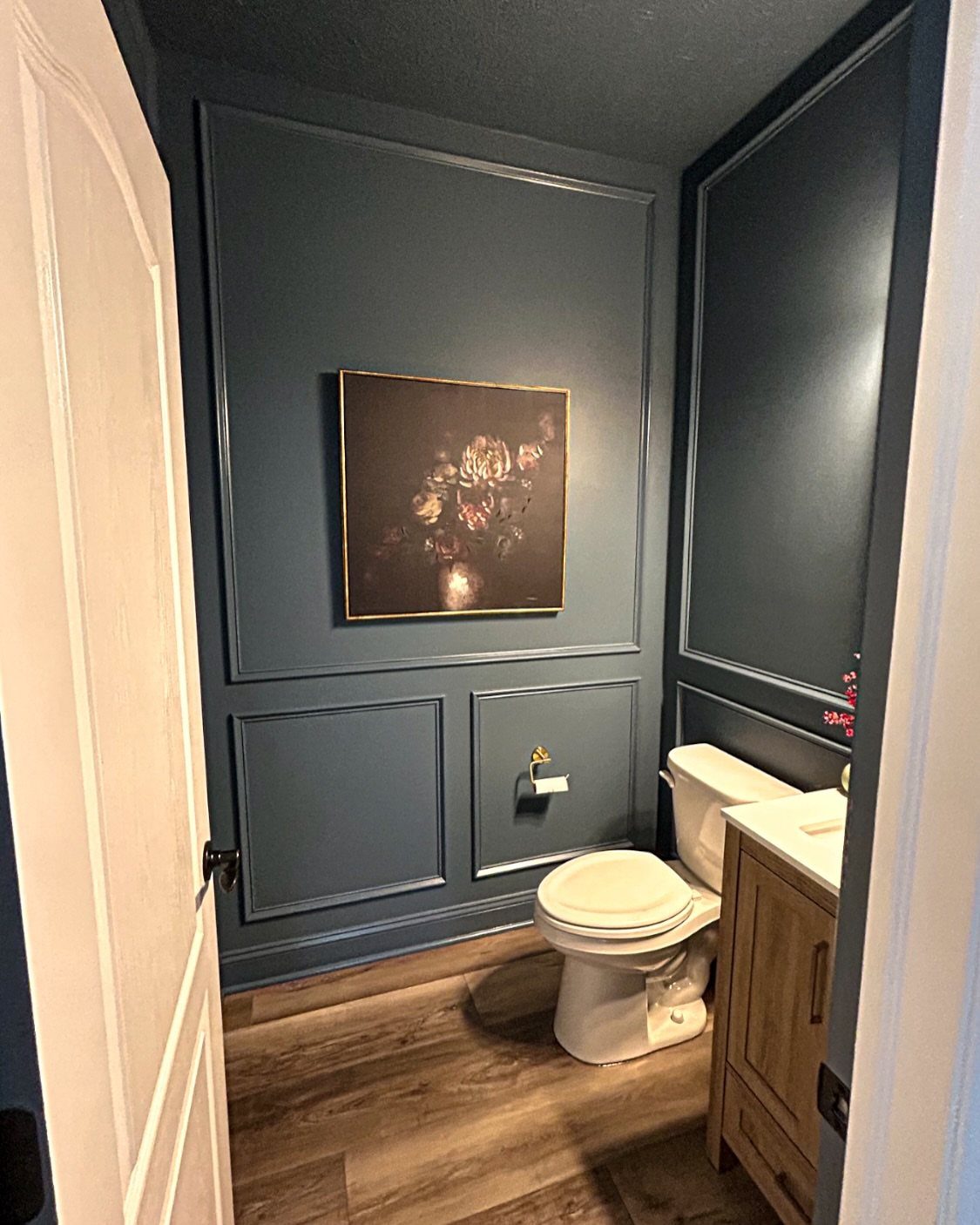 Dark teal bathroom with matching walls and trim, white toilet, and wooden vanity.
