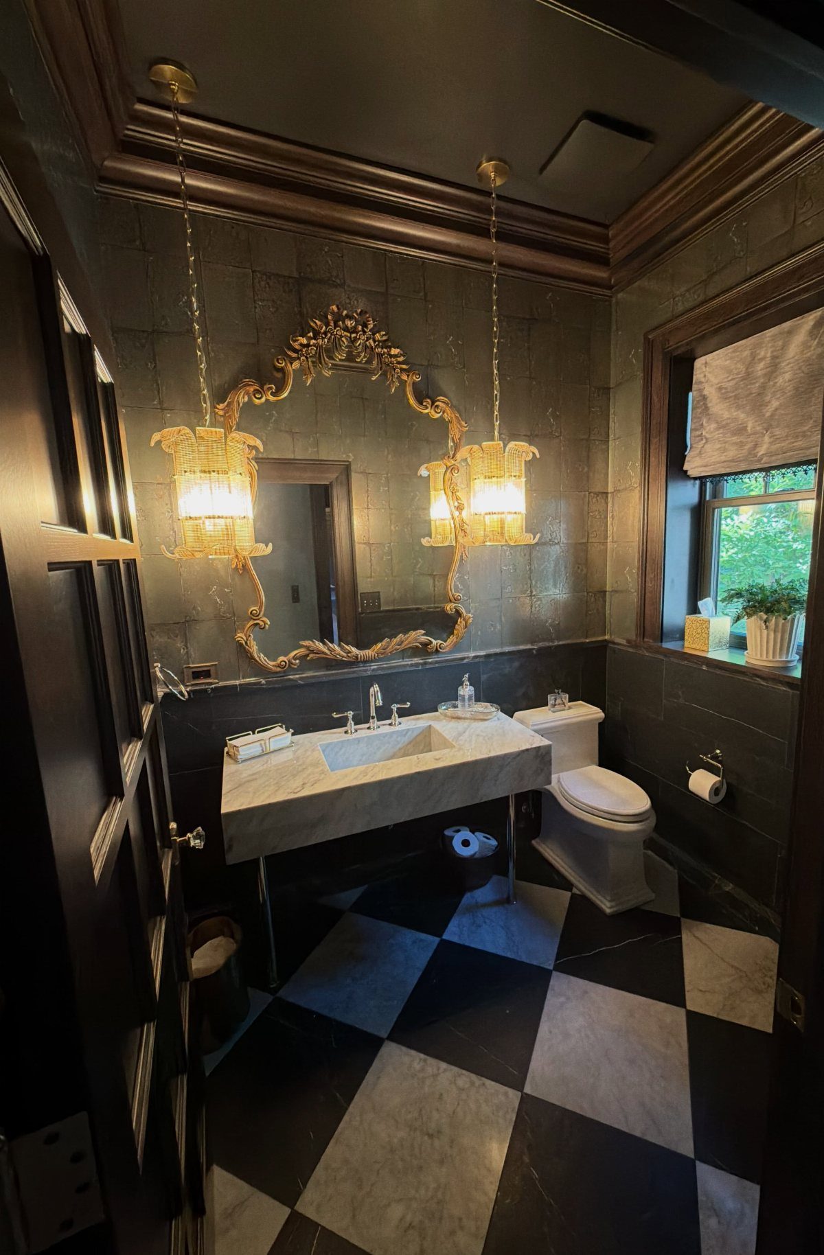 Small bathroom with black and white checkered floors and ornate gold mirror.