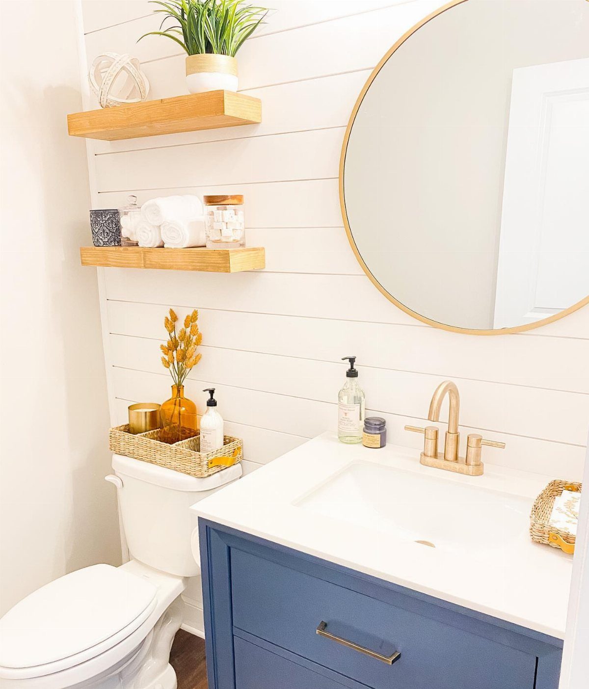 Two light-wood floating shelves on a white shiplap wall in a small bathroom.