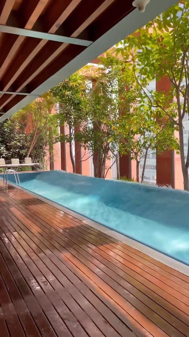 Blue swimming pool with a wooden deck and surrounding green trees.