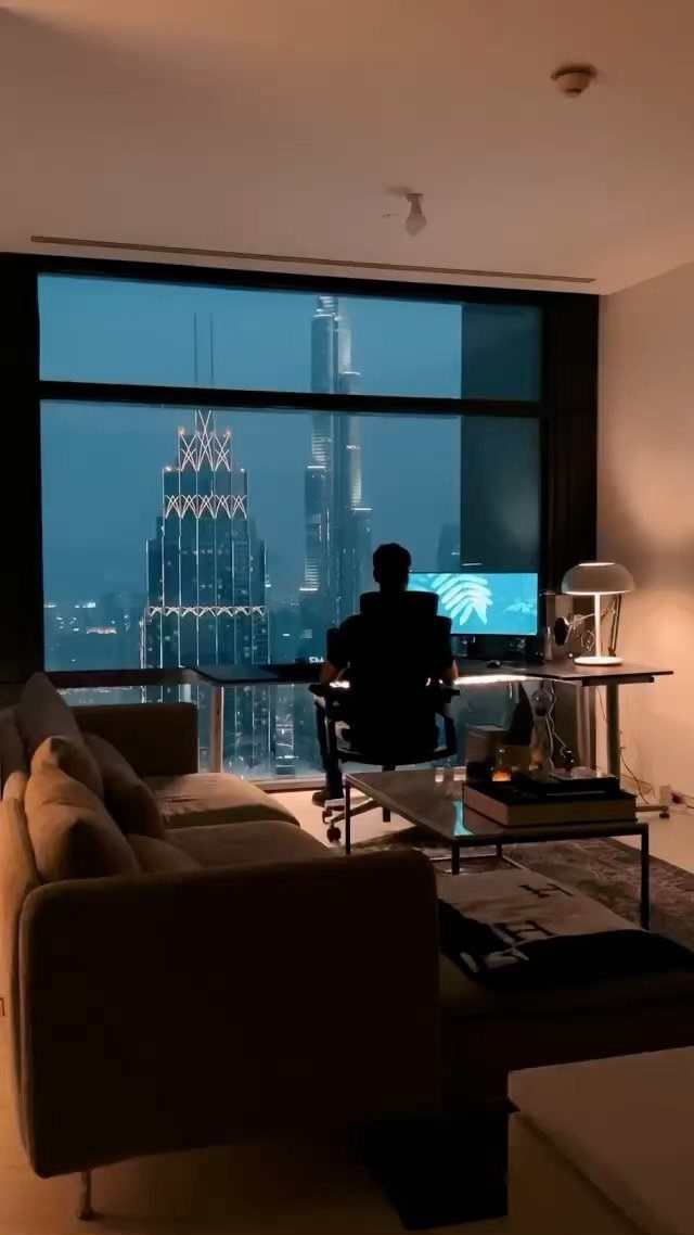 Modern apartment interior with a person at a desk overlooking illuminated city skyscrapers