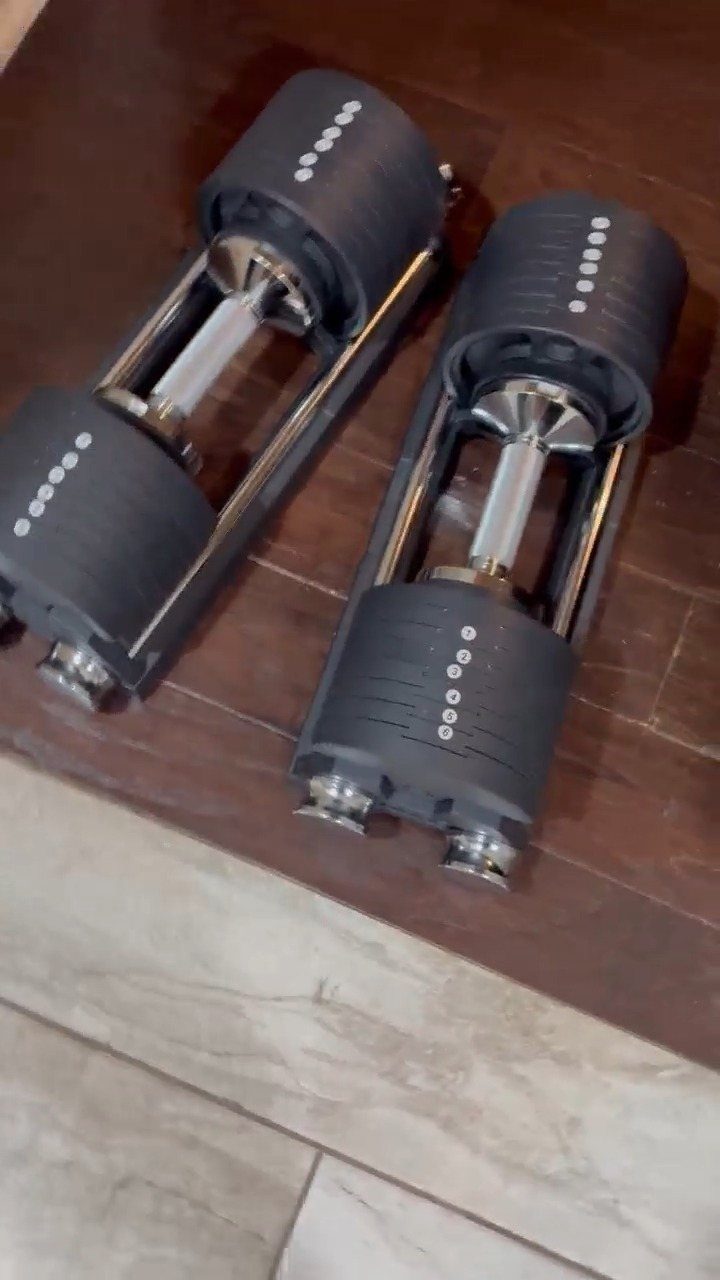 Two black adjustable dumbbells resting on a dark brown wooden floor surface.