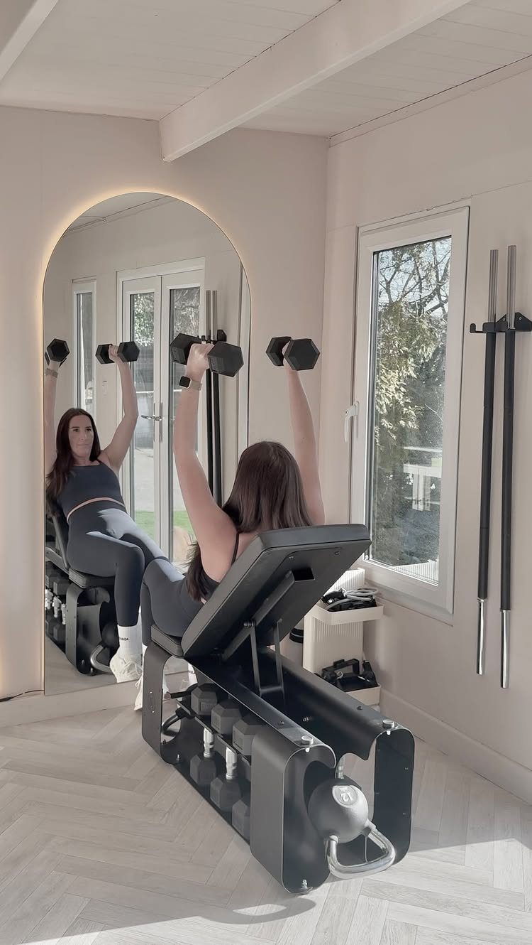 Woman lifting dumbbells on a black adjustable weight bench in a home gym.