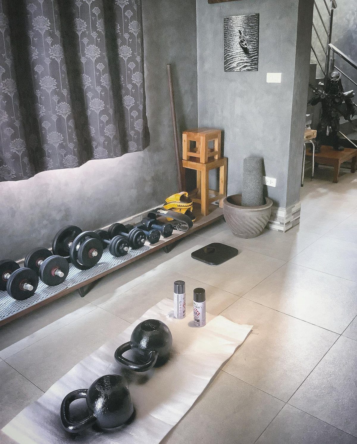 Home gym equipment including dumbbells on a rack and kettlebells on a white mat.