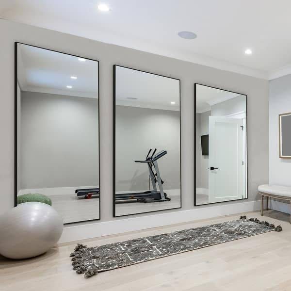 Three large black-framed mirrors on a gray wall in a home gym setting.