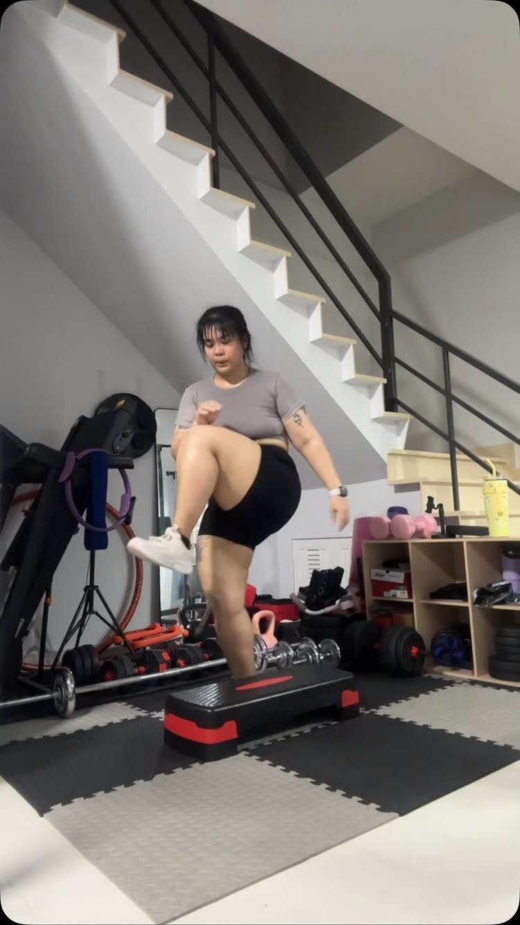 Woman exercising on an aerobic stepper over grey rubber flooring in a home gym.