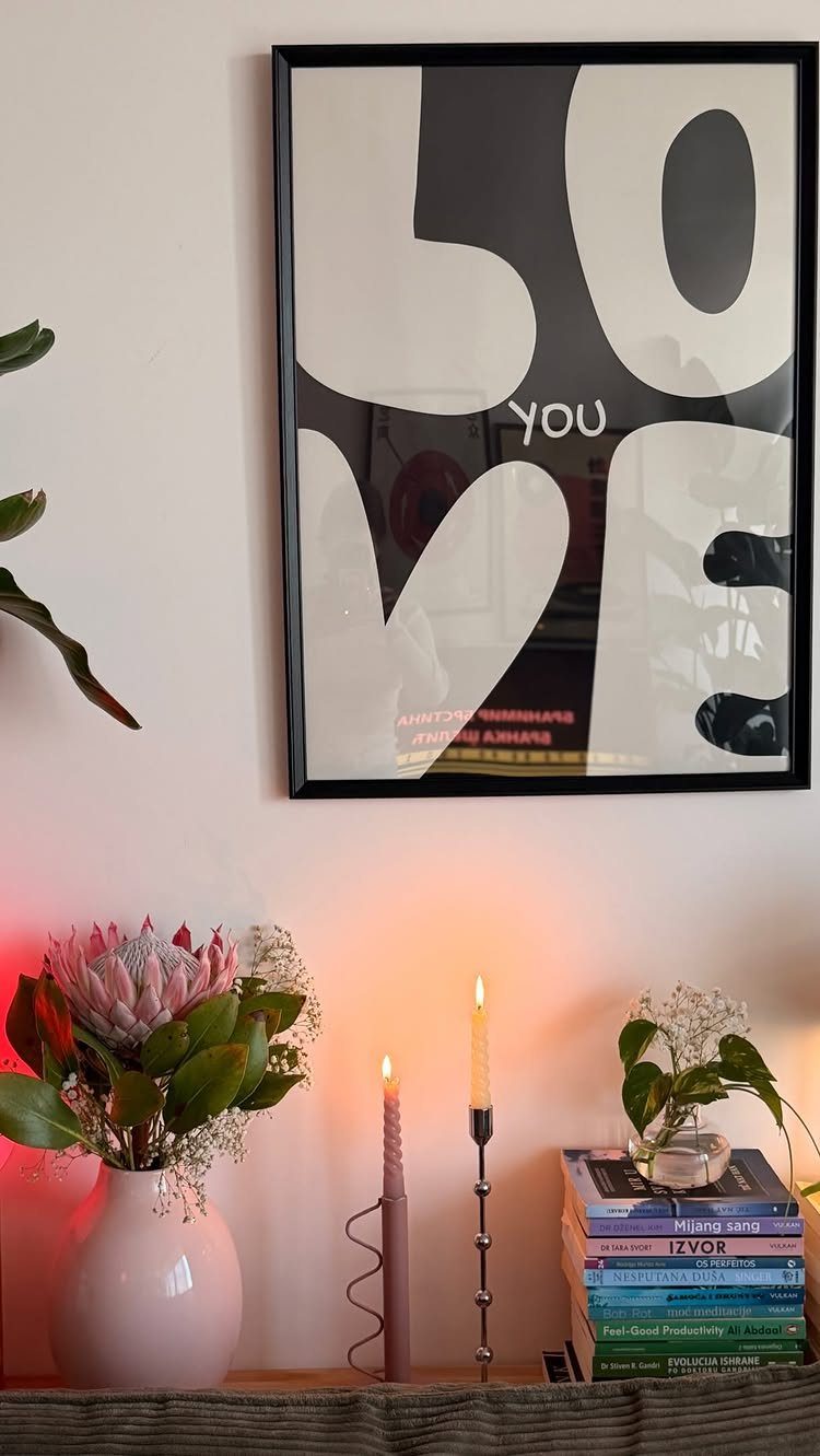 Framed love art print above a shelf with candles, flowers, and books.