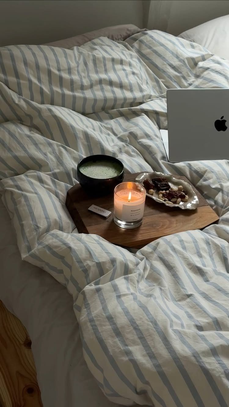 Cozy bed with striped linens, a wooden tray with matcha, candle, and laptop.