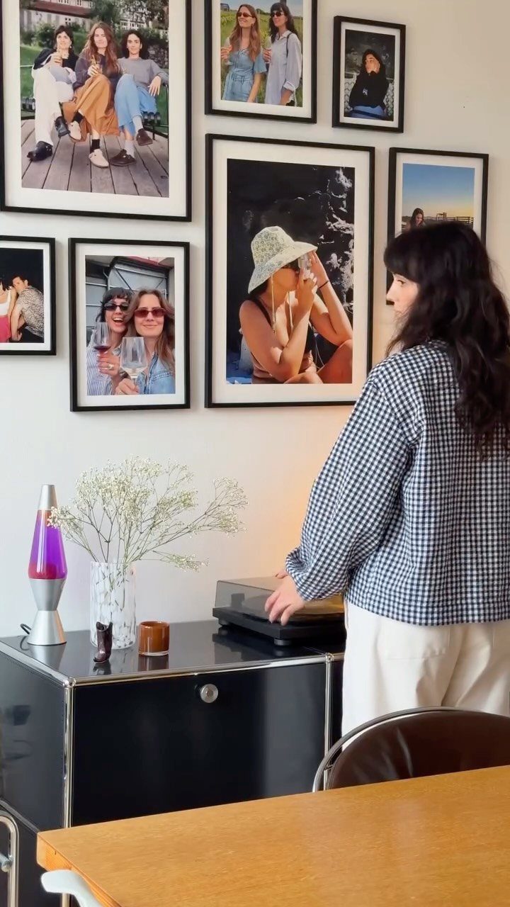 Woman standing in front of a gallery wall with multiple framed photographs.