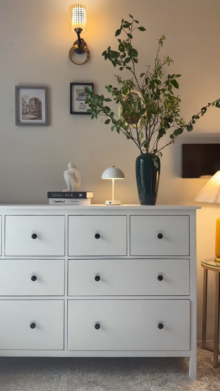 White wooden dresser with black knobs and decorative items on top against a wall