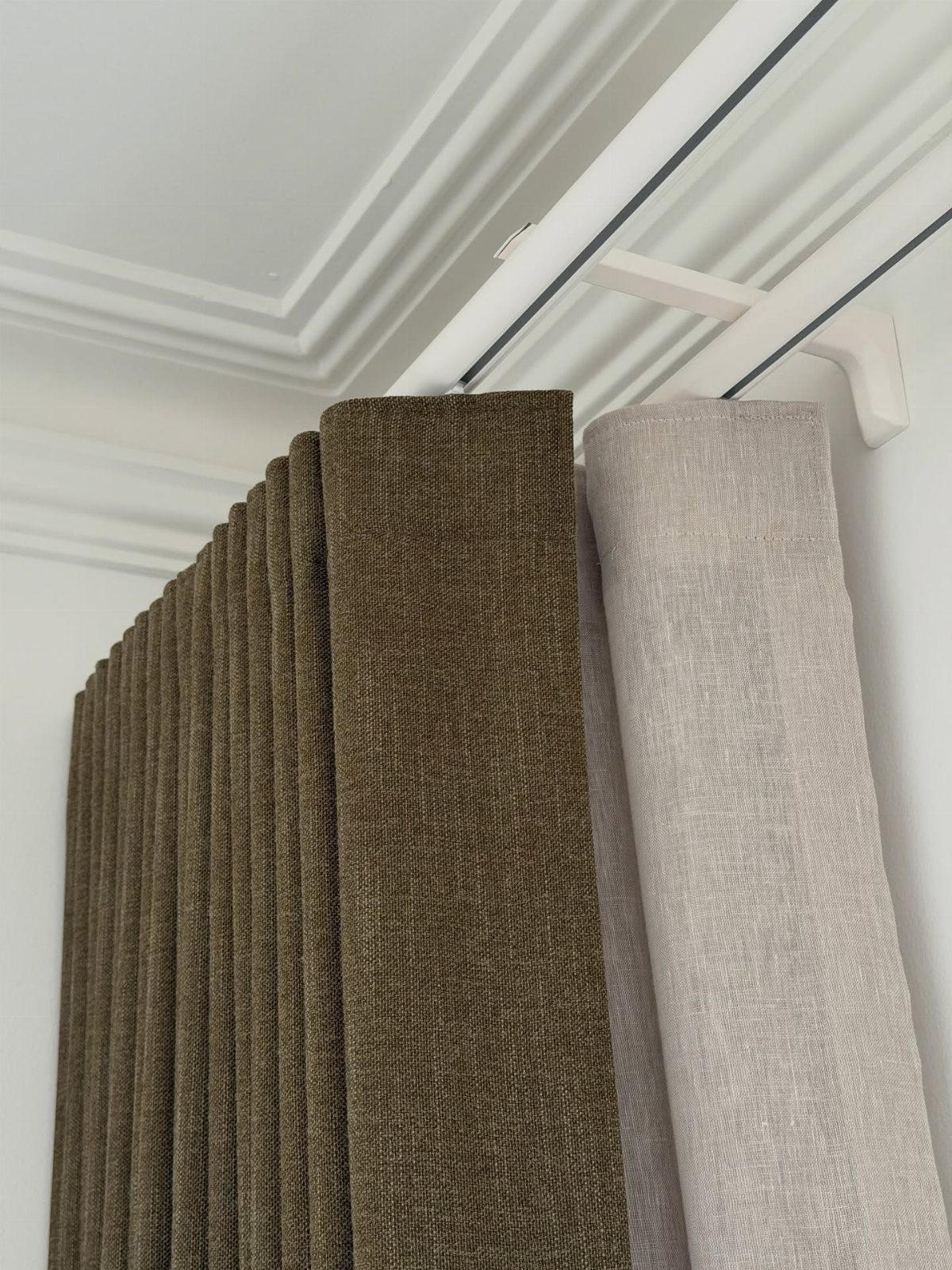Olive green and grey curtains hanging from a rail mounted to the ceiling.