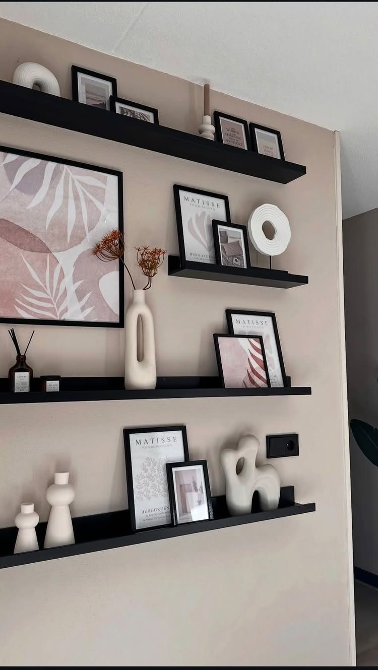 Black floating shelves on a beige wall holding framed art and white vases.