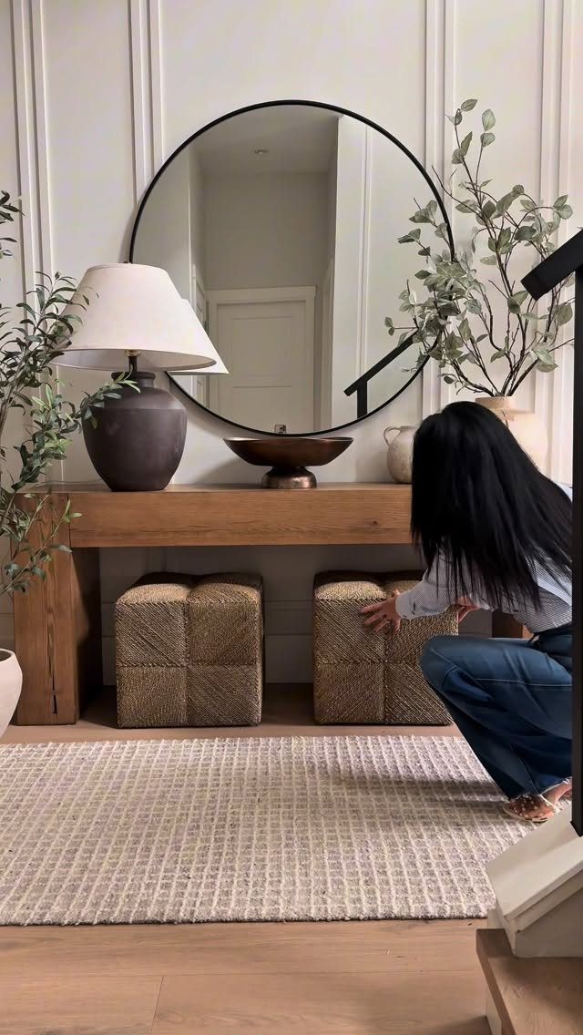 Woven square ottomans tucked under a wooden console table in a bright room.