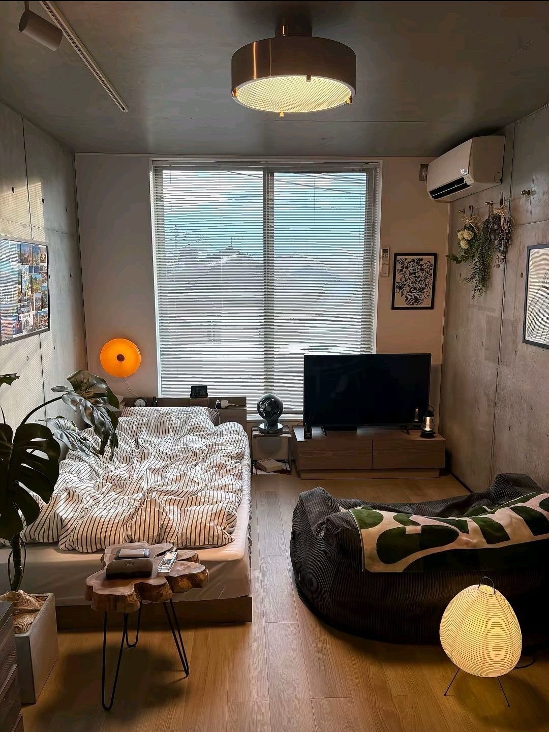 Small studio apartment with a bed, bean bag, and TV in a concrete room.