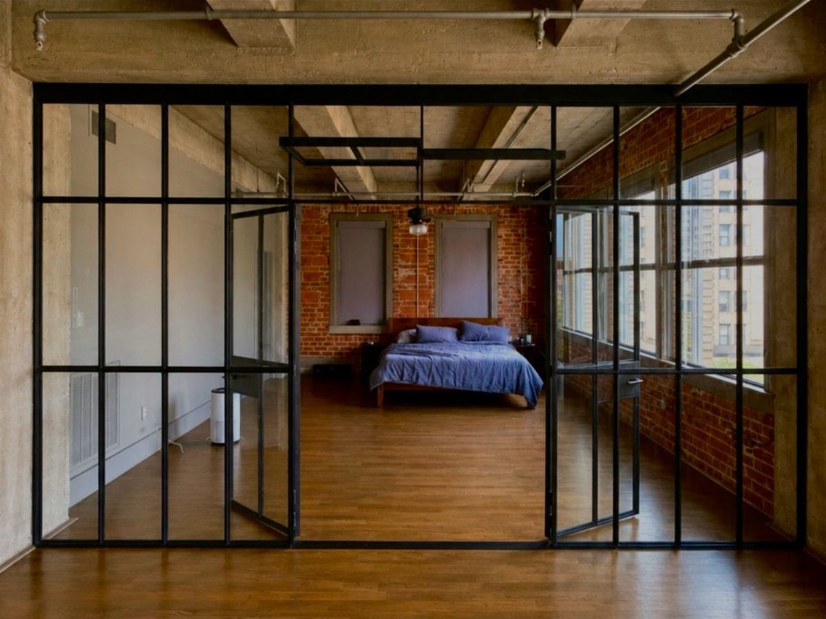 Bedroom with red exposed brick walls viewed through a black glass partition wall.