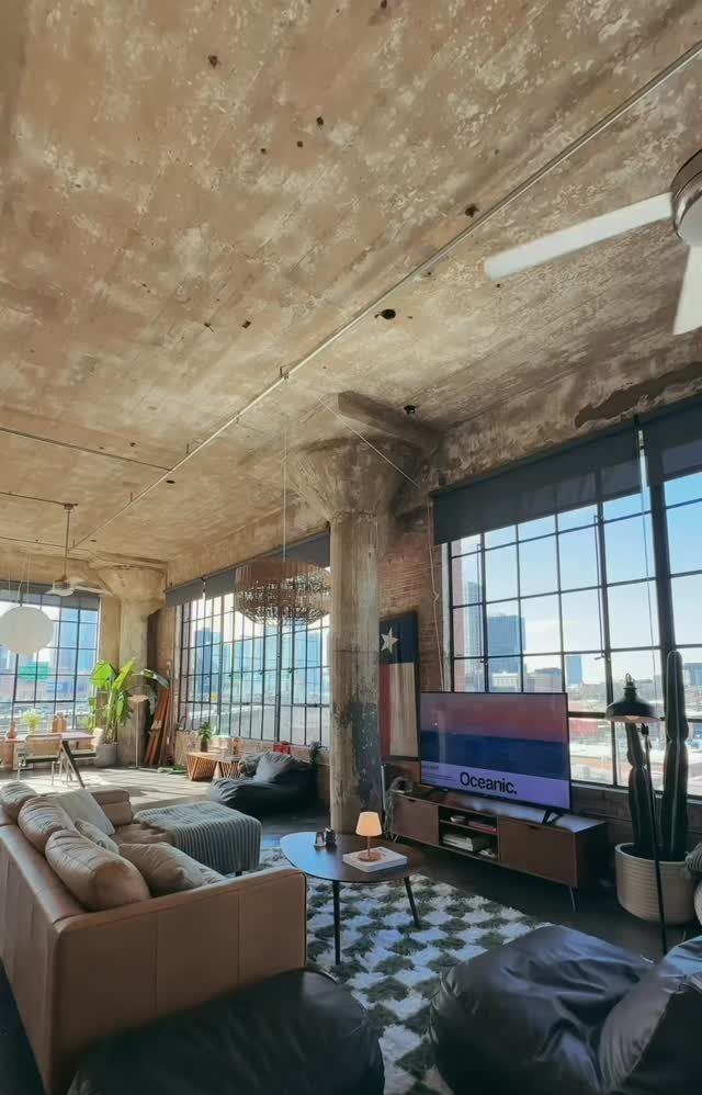 Industrial loft living room with high concrete ceilings and large city-view windows.