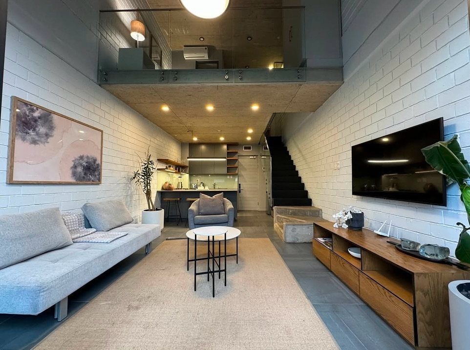 Modern loft living room with white brick walls and a mezzanine level above.
