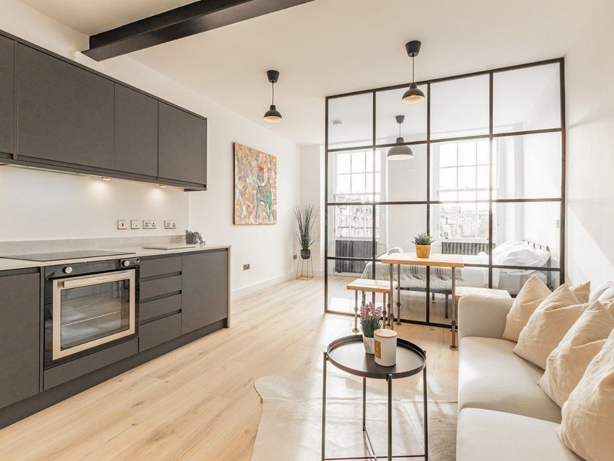 Industrial glass partition separating a modern kitchen and living area from a bedroom