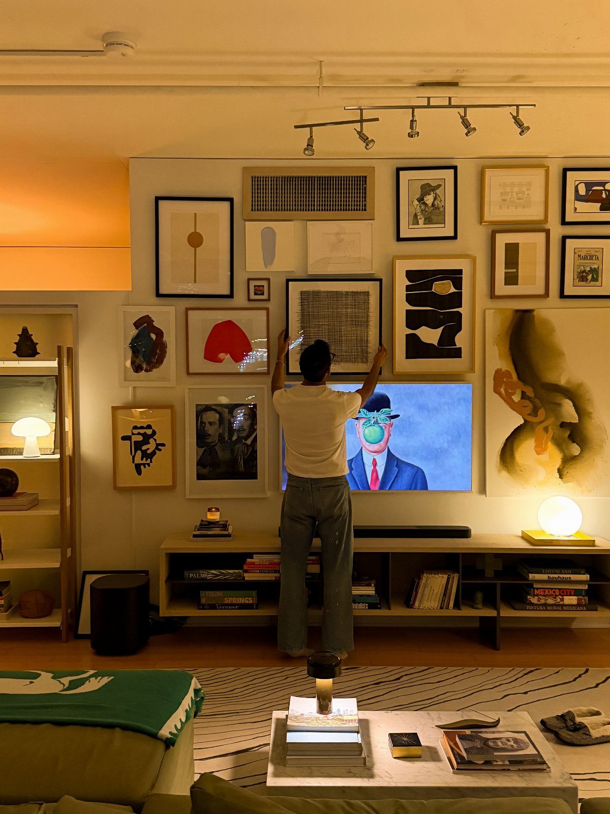 Man arranging a gallery wall of framed art in a modern studio apartment