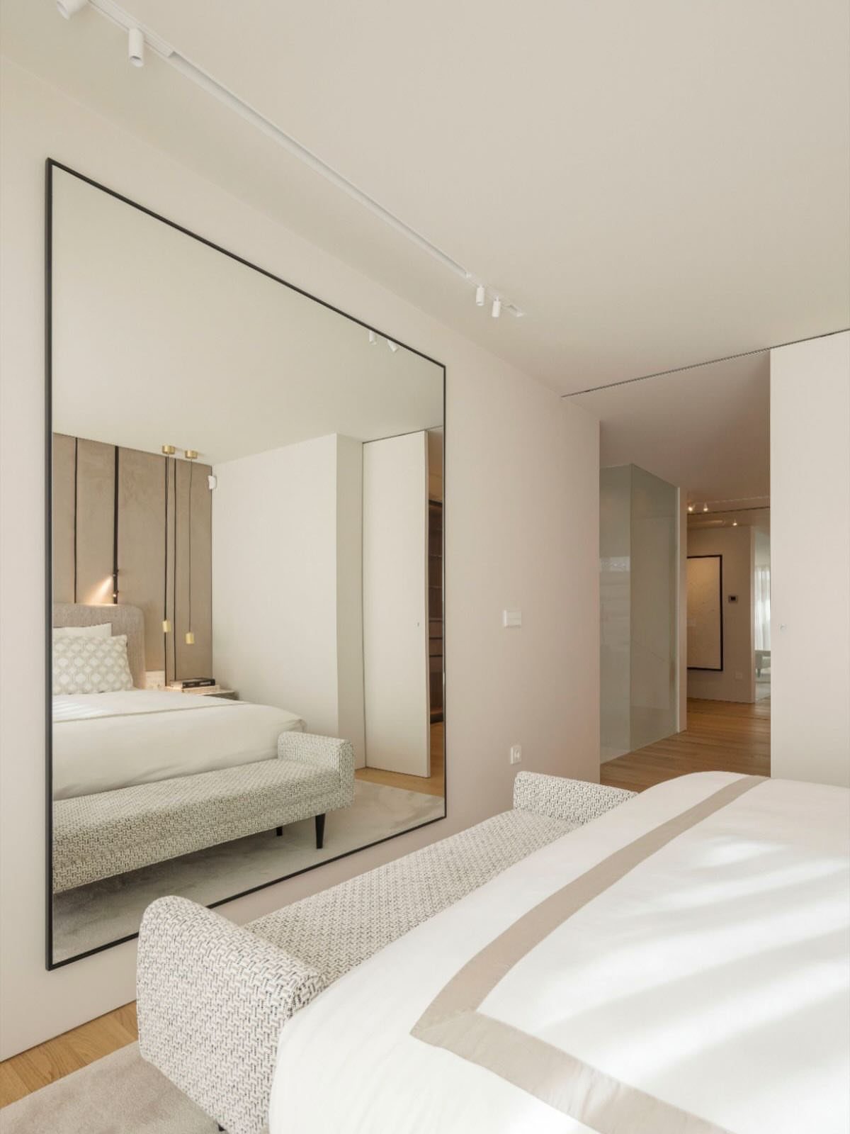 Large rectangular mirror with black frame reflecting a minimalist white bedroom setup