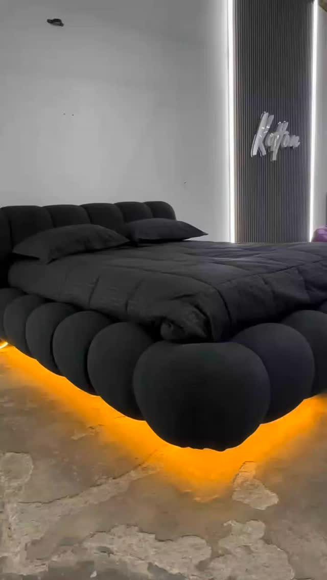 Black tufted bed with orange under-glow lighting in a modern minimalist room.