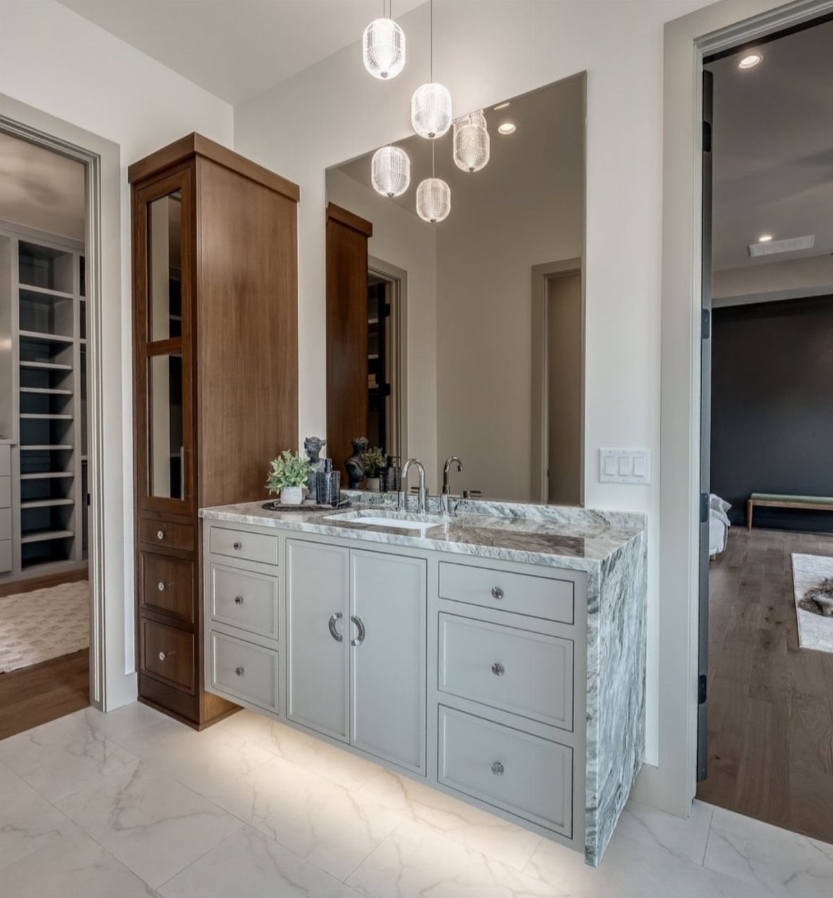 White bathroom vanity with marble countertops and a tall wooden storage cabinet.