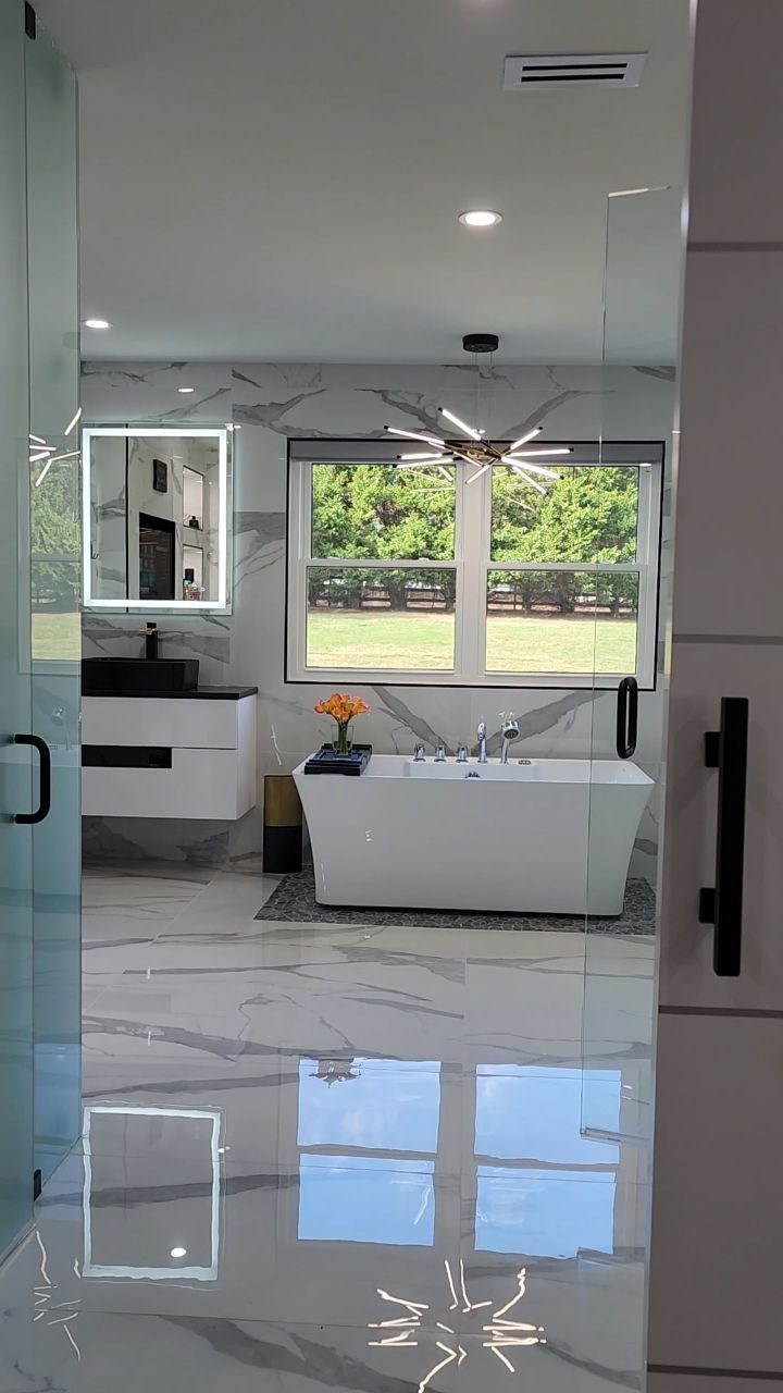 White freestanding bathtub in a modern marble bathroom with a floating vanity.