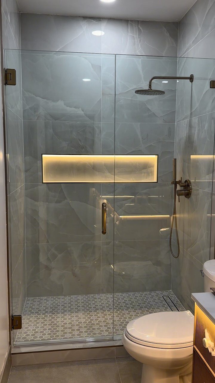 Walk-in shower with marble walls and a rectangular backlit recessed shower niche.