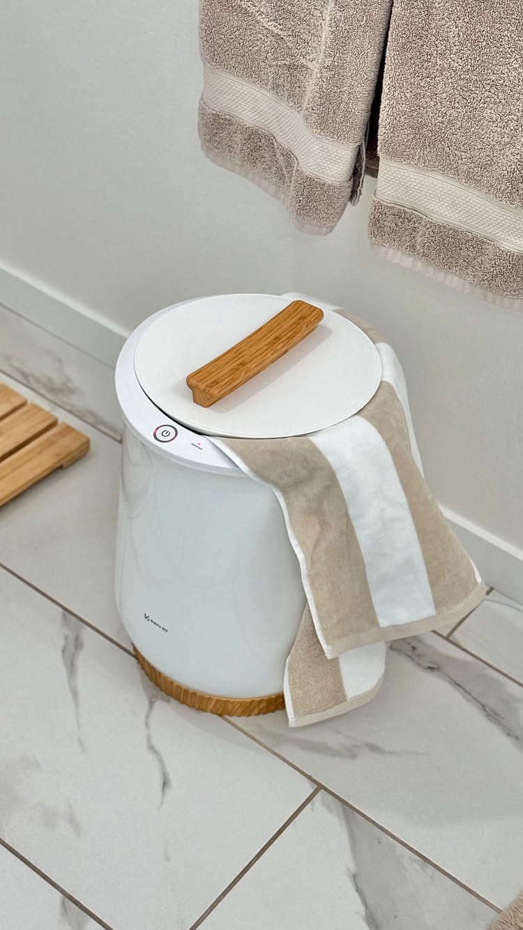 White cylindrical towel warmer with wooden accents on a white marble bathroom floor.