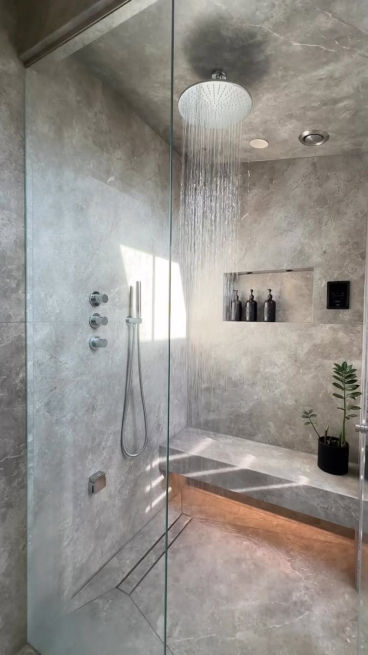 Modern walk-in shower with grey marble tiles, rain showerhead, and illuminated stone bench.