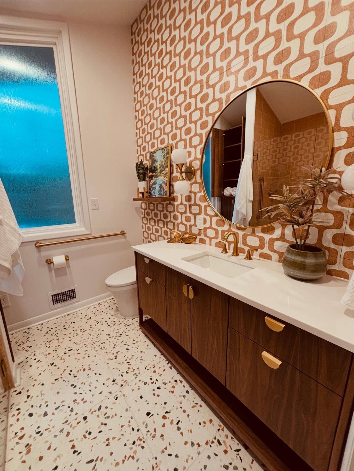Geometric patterned accent wall in a bathroom with wood vanity and terrazzo floors.