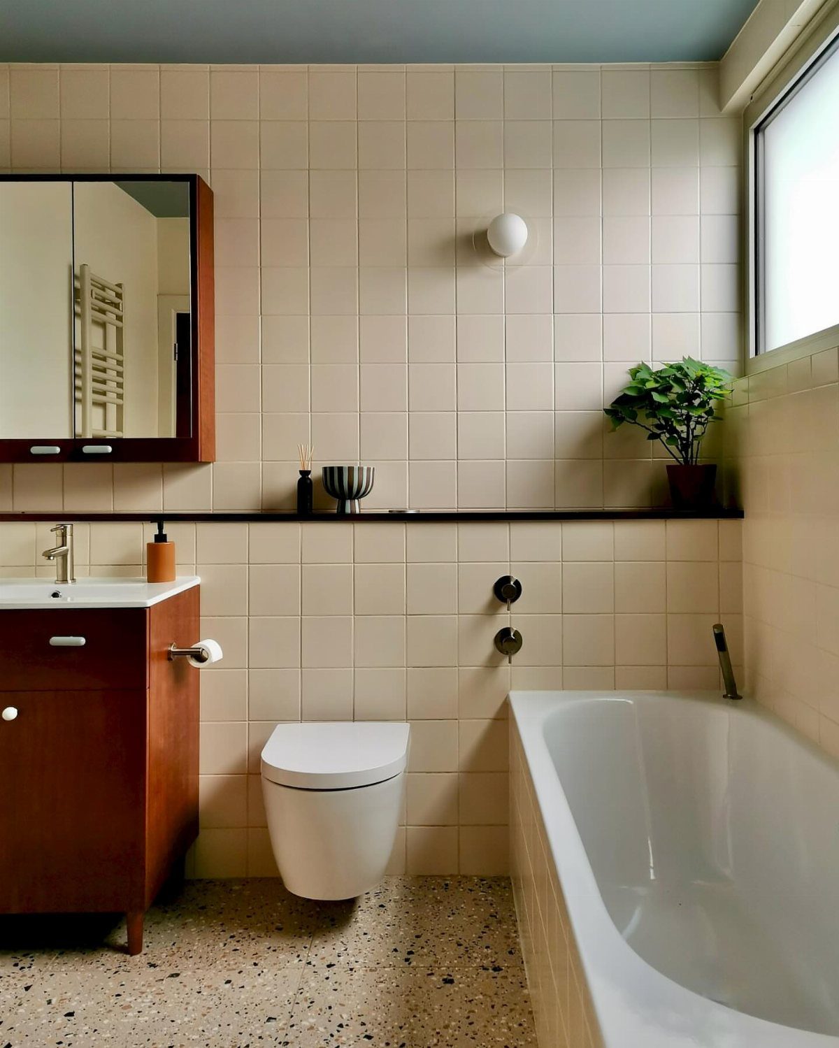 Mid century modern bathroom with wood vanity, beige tiles, and terrazzo flooring.