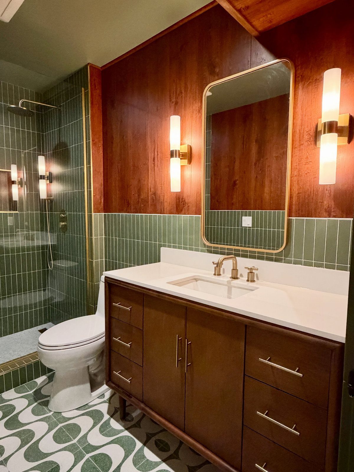 Mid-century modern bathroom with green accent tiles, wood vanity, and geometric flooring.