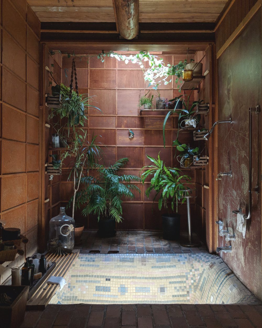 Sunken tiled bathtub in a rustic bathroom with many green plants and skylight.
