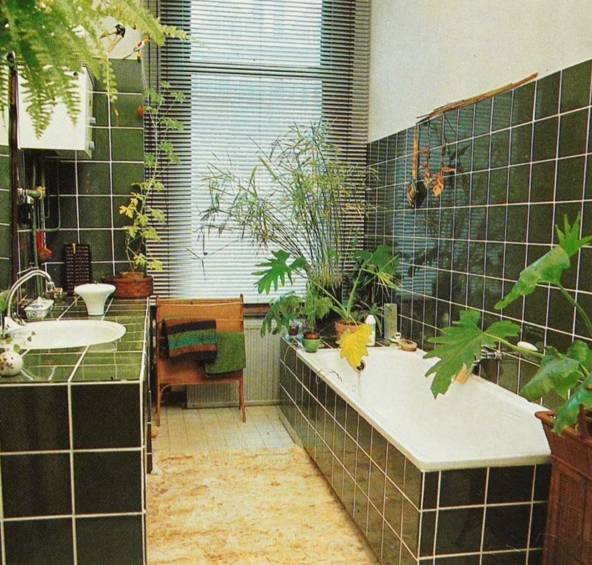 Bathroom with dark green tiles, white bathtub, and various green potted plants.
