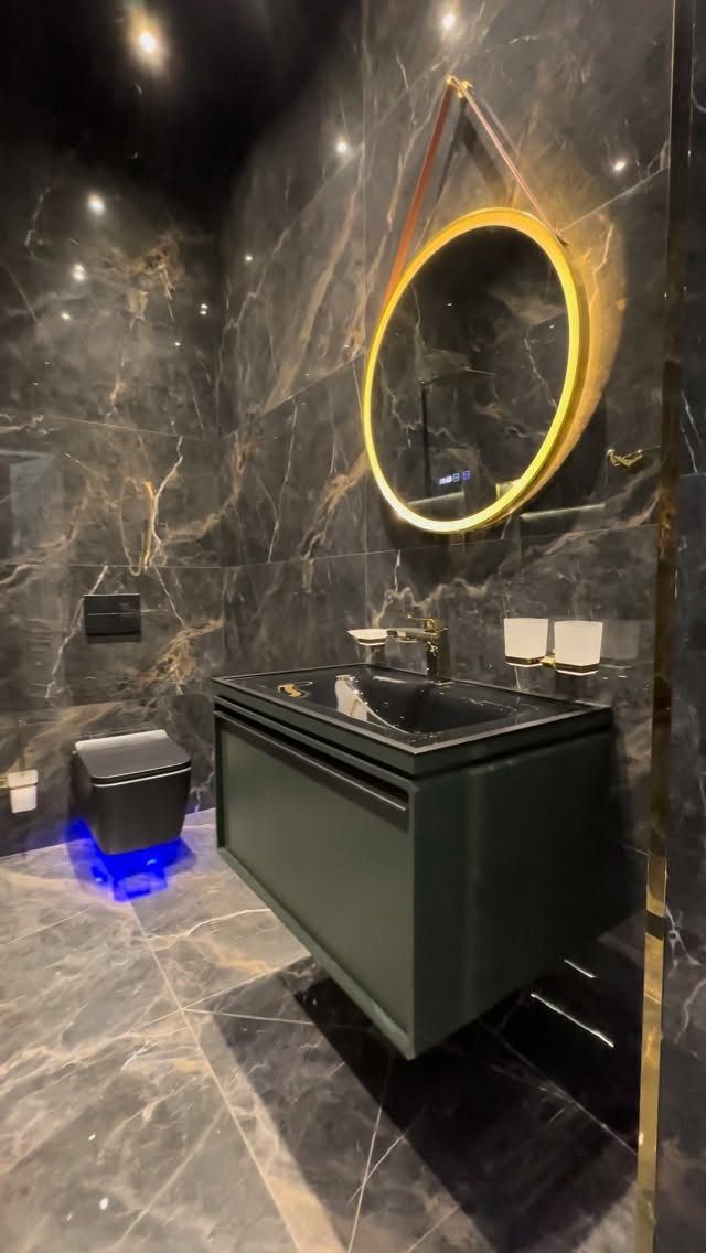 Luxurious bathroom with dark marble walls, black floating vanity, and gold circular mirror.