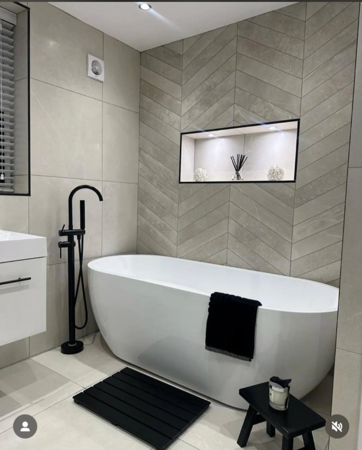 White oval freestanding bathtub in a modern bathroom with grey chevron wall tiles.