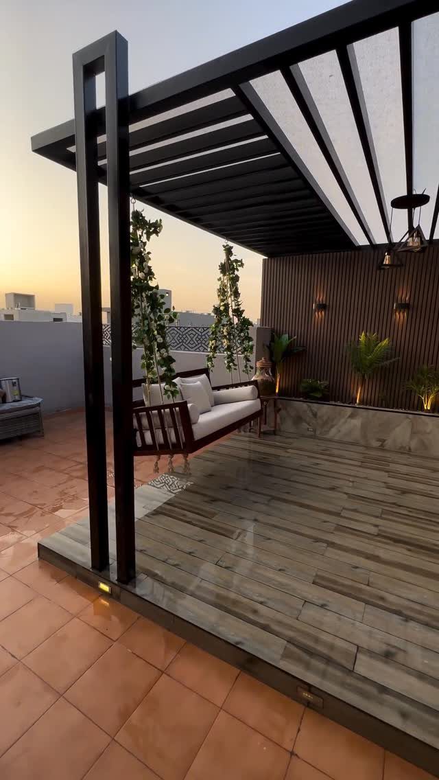 Modern rooftop terrace with a black pergola, white sofa, and lush green plants.