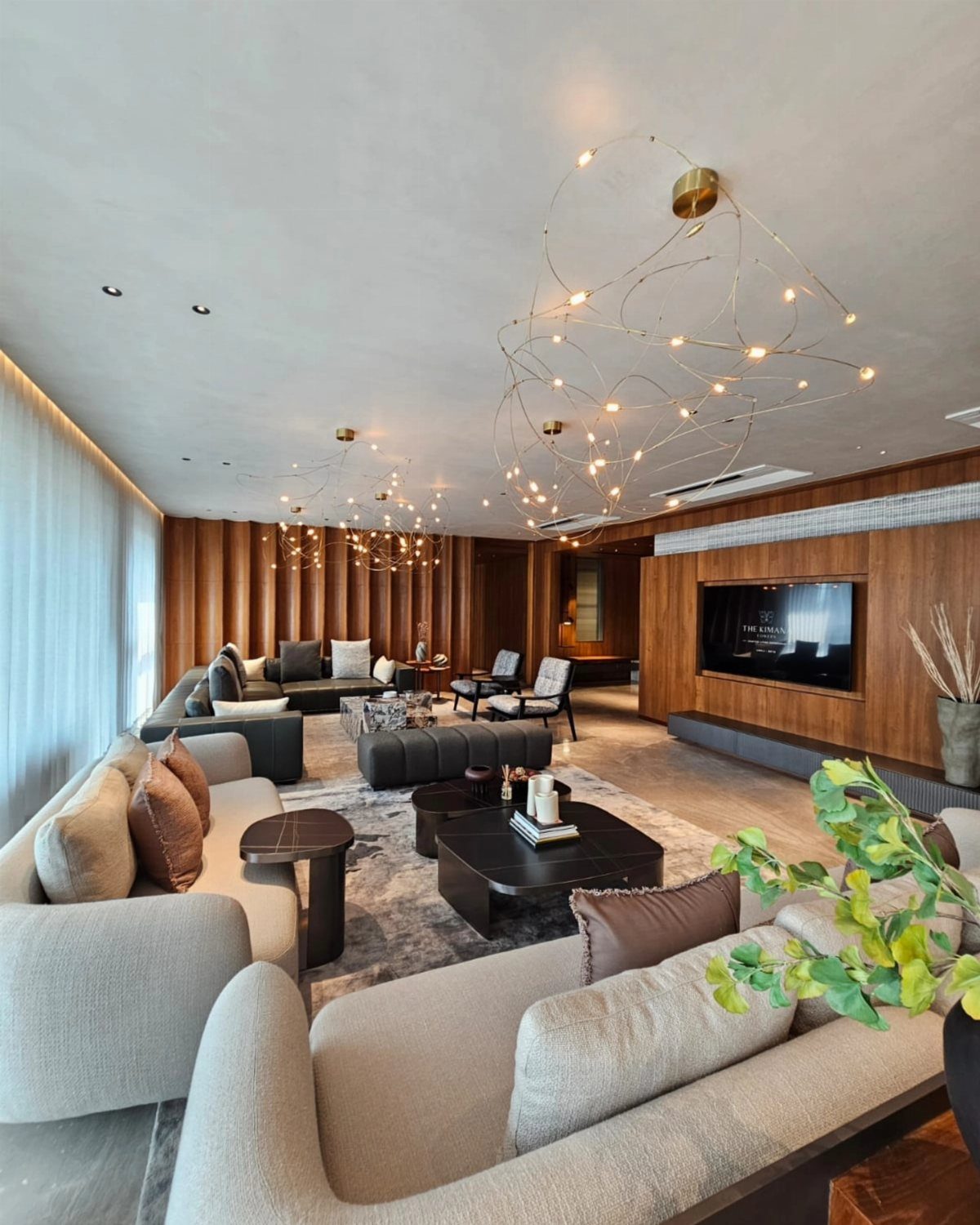Modern living room with beige sofas, wood paneling, and sculptural gold chandeliers.