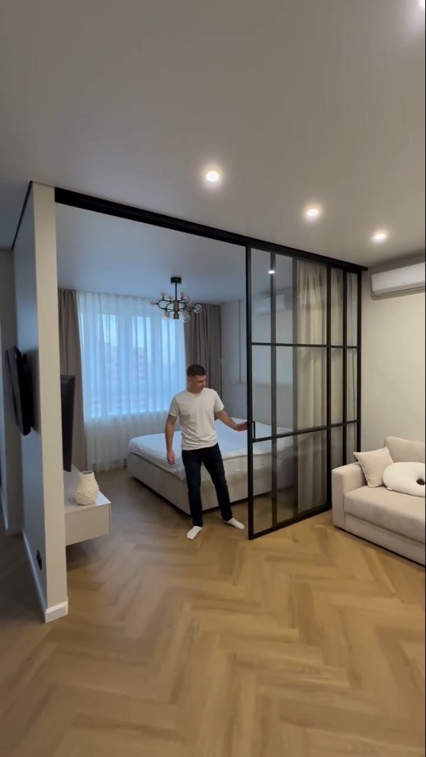 Black-framed glass sliding doors separating a living area from a bedroom in a studio.
