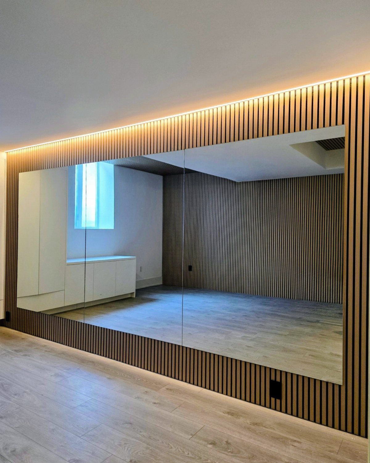 Large wall mirror with wooden slat frame and LED lighting reflecting a modern room