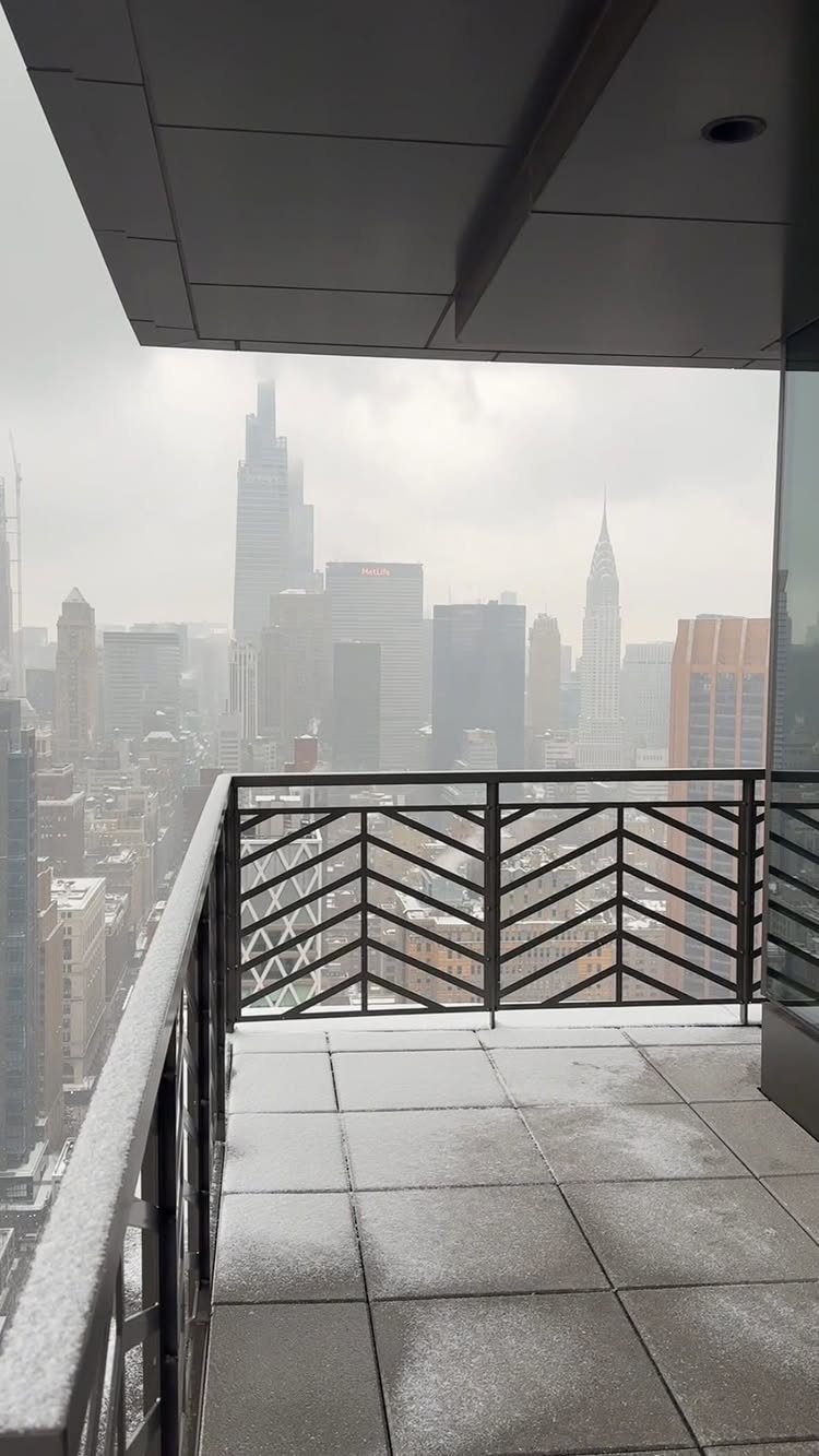 High-rise balcony with black railings overlooking the hazy New York City skyline.