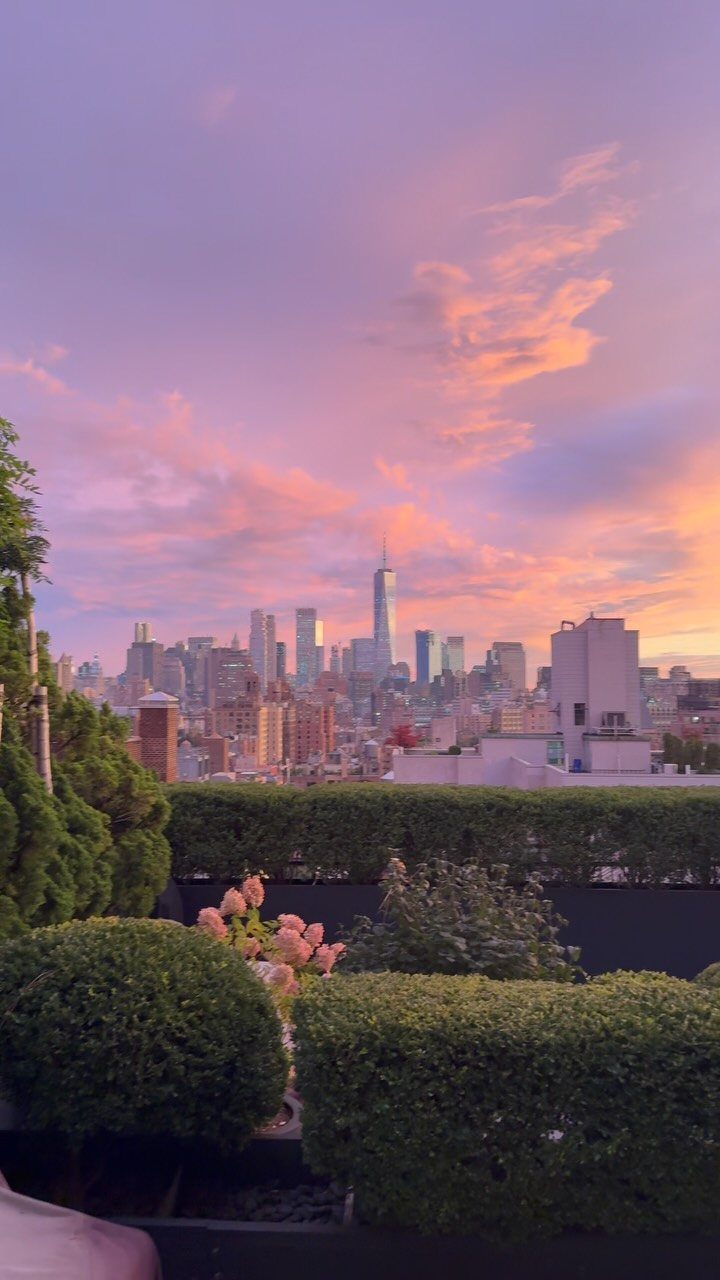 Rooftop terrace with green hedges overlooking the New York City skyline at sunset.