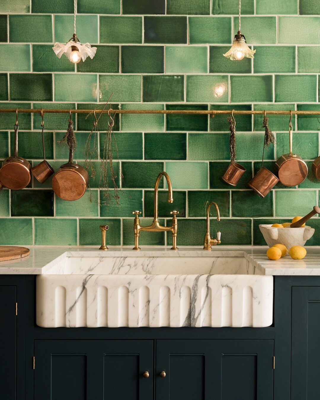 Marble farmhouse sink with brass fixtures against a green tiled kitchen wall