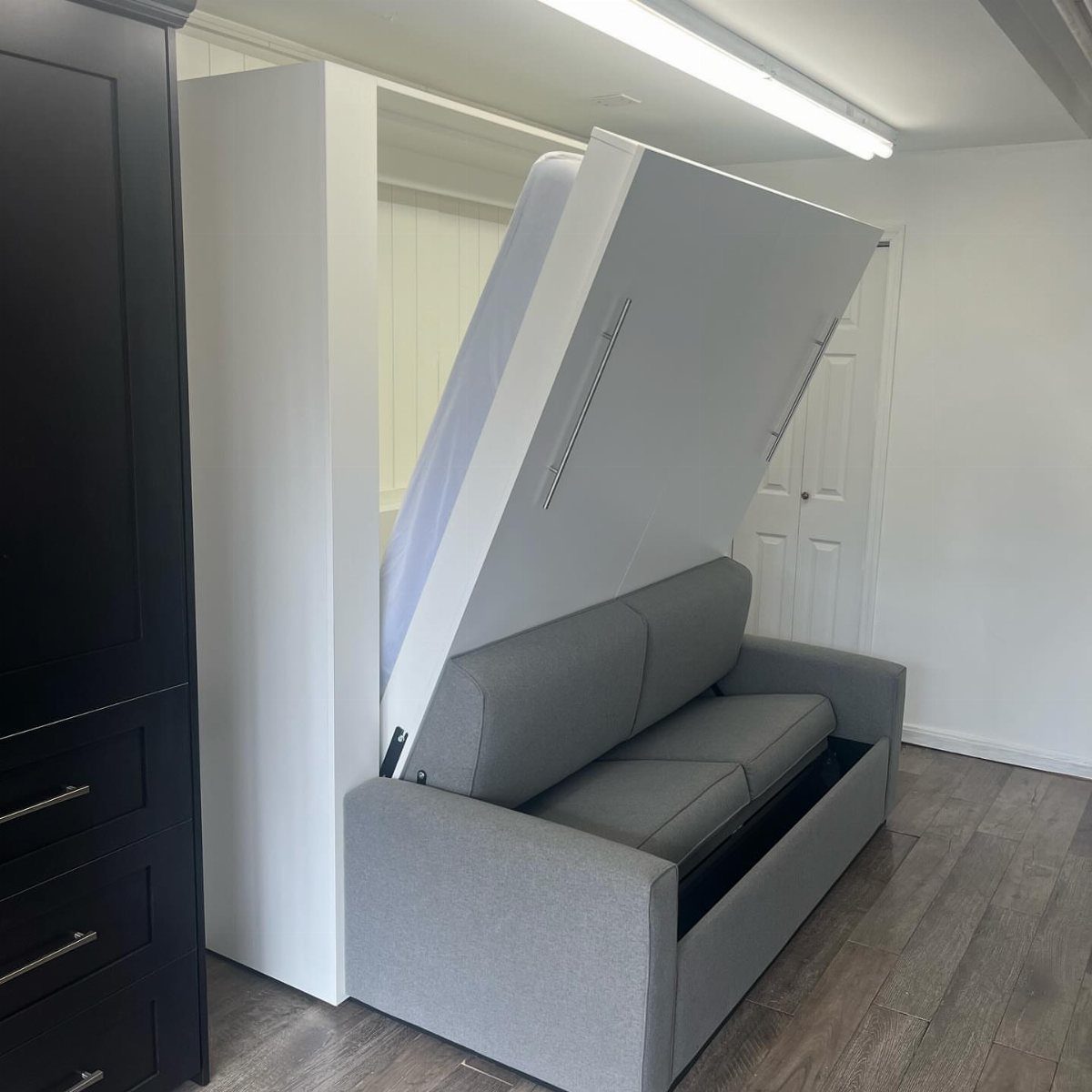 Grey sofa with a white Murphy bed unfolding from a wall unit.