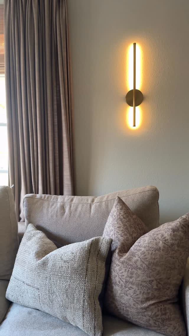 Gold wall sconce lighting a neutral wall above a beige sofa with pillows.