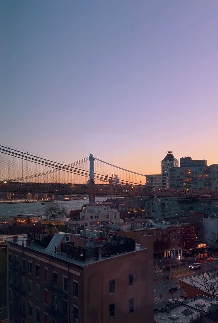 Brooklyn Bridge spanning the river with city buildings under a purple sunset sky.